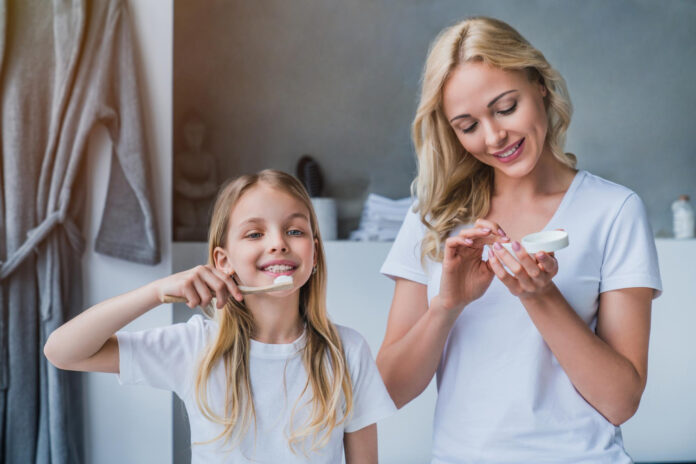 little girl brushing teeth while her mother using cream bathroom